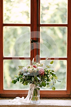 Bridal bouquet of white peonies, roses, pink protea, snowberry, branches of eucalypt tree and white ribbons on the