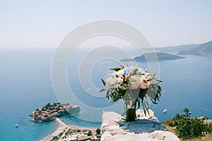 Bridal bouquet of white and pink roses, peonies, hortense branches of eucalypt tree, and white ribbons on the stone