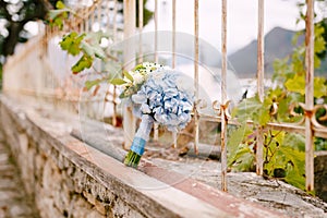 Bridal bouquet of white roses, eucalyptus tree branches, blue hortensias, green asters and blue ribbons on the brick photo