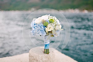 Bridal bouquet of white roses, eucalyptus tree branches, blue hortensias, green asters and blue ribbons on the pier by photo