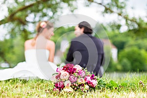 Bridal pair with bouquet sitting on meadow