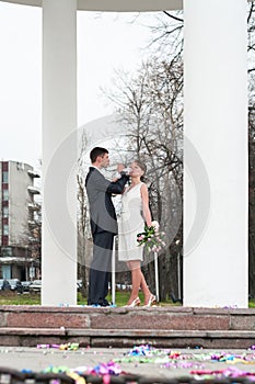 Bridal pair drinking champagne from wine glasses, bride and groom are between white columns outdoor