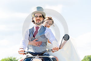 Bridal pair driving motor scooter wearing gown and suit