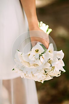 Bridal wedding bouquet with white flowers. Bride in white dress holding classic callas bouquet on brown background