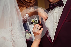 Bride adjusts carefully a boutonniere on groom& x27;s jacket