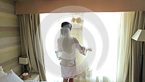 Bride admiring her beautiful wedding dress in front of the window.