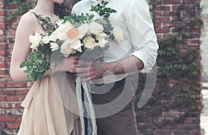 Bride with amazing bouquet of fresh delicate flowers and groom hugging on street