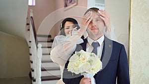 the bride approaches the groom from behind and closes his eyes.