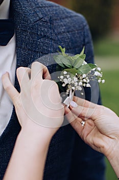 The bride attaches a boutonniere to the groom`s jacket