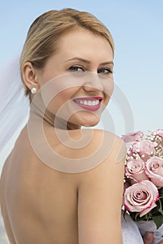 Bride In Backless Dress With Flower Bouquet Against Clear Sky photo