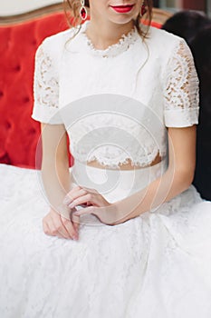 Bride in beautiful dress with red lipstick on velvet sofa. Hands close-up. Excitement before wedding.