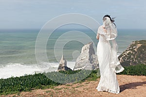 Bride in a beautiful white dress on a cliff by the ocean