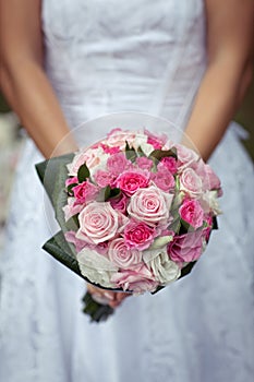 Bride in beautiful white dress is holding colorful wedding bouquet of pink, white, and purple roses
