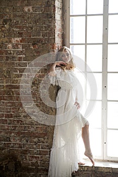 Bride in beautiful white dress posing against the window