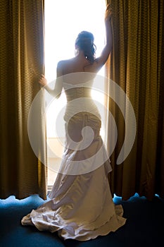 Bride from behind looking through curtains