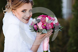 The bride with blond hair and French manicure smiles and shows her beautiful bouquet. Close view of the bride`s face