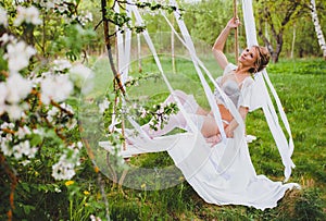 Bride with blond hair in white negligee and stockings sitting on a rope swing