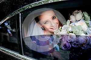 Bride with blue eyes holds tender wedding bouquet sitting in the car