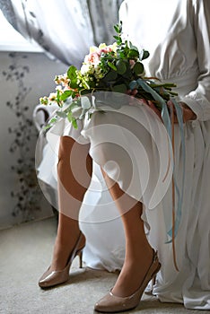 Bride with a bouquet in front of the window waiting for the groom