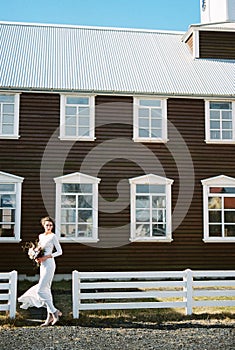 Bride with a bouquet stands near a brown wooden church. Iceland