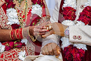 Bride with bridal jewelry and henna decoration on her hand attaches ring to her groom`s finger