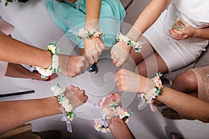 The bride and bride`s maidens are sitting in a circle and holding their fists. Hands with flower bracelets.