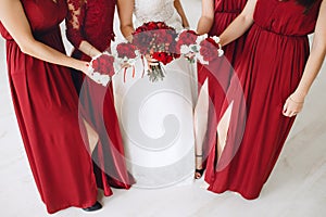 Bride and bridesmaids with red bouquets of roses.