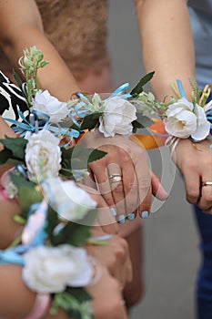 The bride and bridesmaids stand in a circle and hold hands with white flower bracelets, corsages. Bachelor girls party