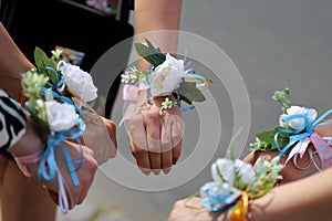 The bride and bridesmaids stand in a circle and hold their hands with white flower bracelets, corsages. Bachelor girls party