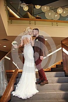 Bride in a chic long dress with a train and the groom stand on big stairs, couple in love hugs on stairs kiss and look at each