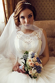 Bride with dark hair in luxurious lace wedding dress with bouquet of flowers