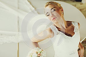 Bride daydreams standing leaned on a wite piano photo