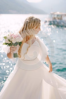 A bride in a delicate dress with a bouquet in her hand stands on a pier in the Bay of Kotor