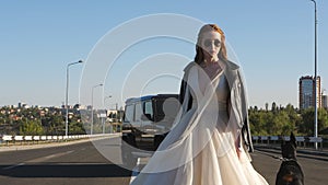 The bride with a Doberman in a leather jacket and glasses turns to the camera on the roadway.