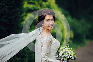 bride in a dress standing in a green garden and holding a weddin