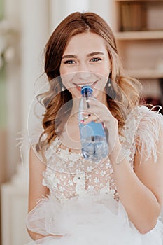 Bride drinks water from bottle through straw so as not to spoil makeup