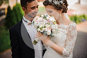 Bride enjoys the scent of a wedding bouquet, the groom stands beside smiling