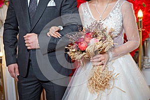 The bride entered the groom`s armpit and held a bouquet of flowers . dried coral reach pink wheat cotton flower bridal bouquet