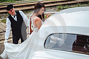 Bride entering classic car and driver holding dress