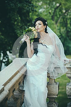 Bride in fashion white dress and veil. Sensual woman with wedding bouquet. Woman with flowers on balcony. Beauty girl