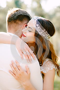 The bride gently hugs the groom in the park and smiles, close-up