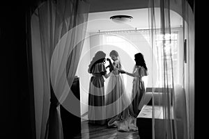 A bride getting dressed for the wedding and being helped by her bidesmaid in a dark room.