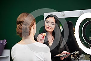 Bride getting ready for wedding. Professional make-up artist applying blush on female clients` face with big makeup brush. Work