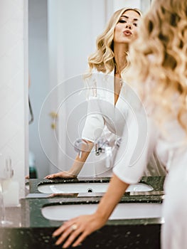 Bride girl in a white peignoir is preparing for the holiday, looking at herself in the mirror in the bathroom romantic photo