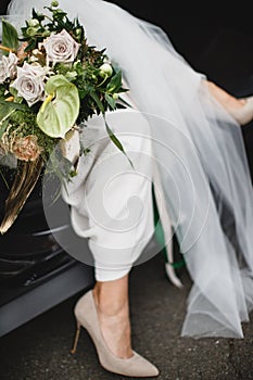 The bride is going out of the car with a big flover bouquet closeup