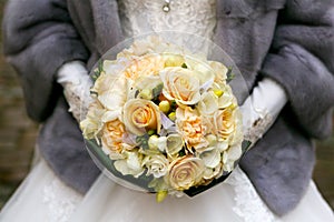 Bride in a gray fur coat holding a bridal bouquet of roses. Winter wedding