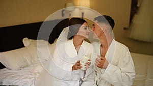 Bride and groom barefoot drinking coffee cups in bed at morning together.
