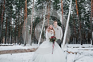 Bride and groom with a bouquet are posing on background of the snowy forest. Winter wedding. Artwork