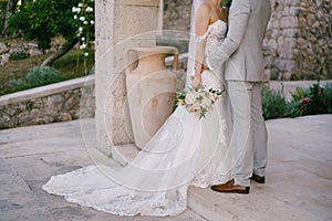 Bride and groom with a bouquet stand near a beautiful stone arch