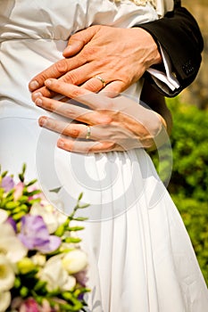 Bride and groom with bunch of flowers. Hands of bride and groom with rings.